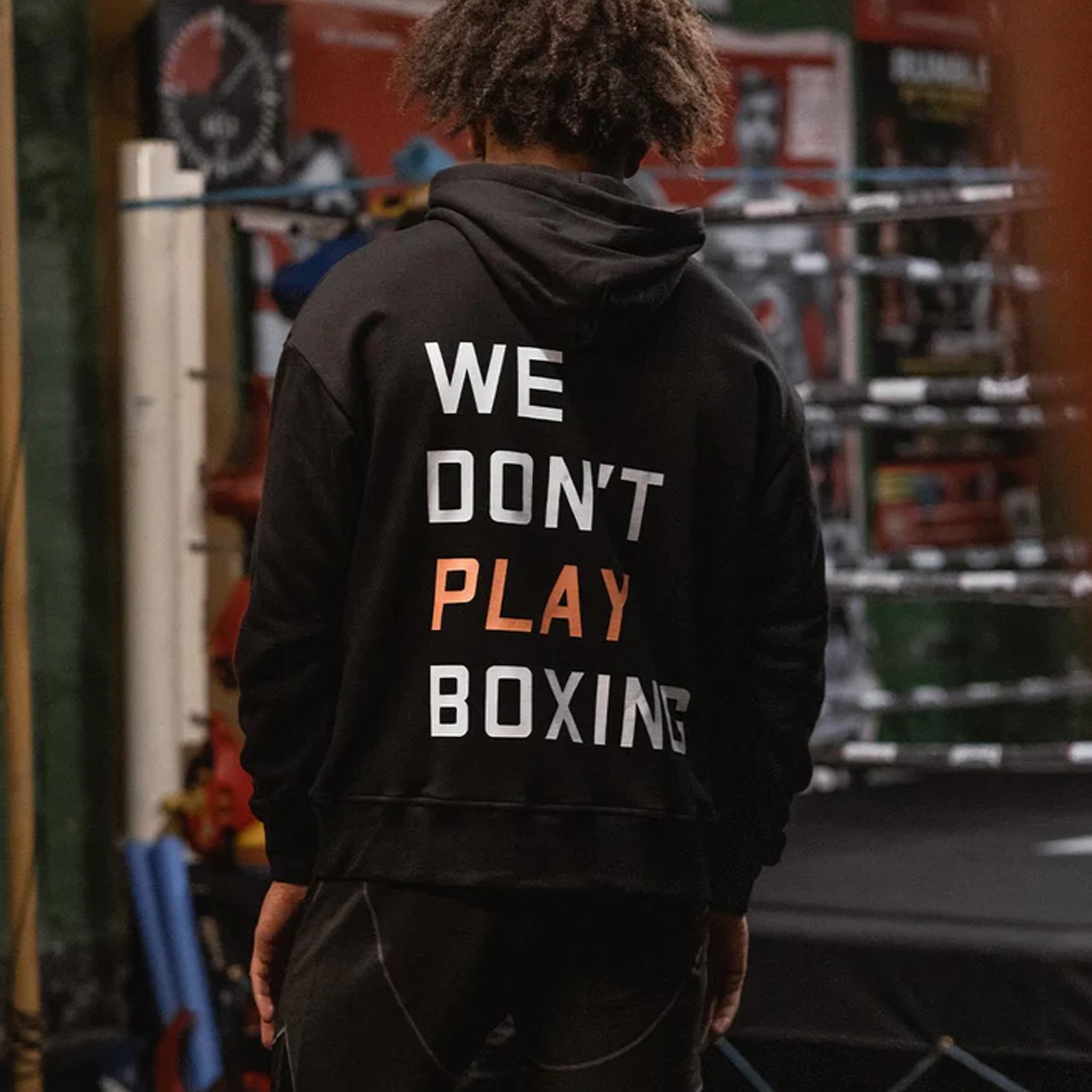 boxraw we dont play boxing oversized hoodie black with large WE DONT PLAY BOXING text on back model is standing ina boxing gym displaying the back of the hoody