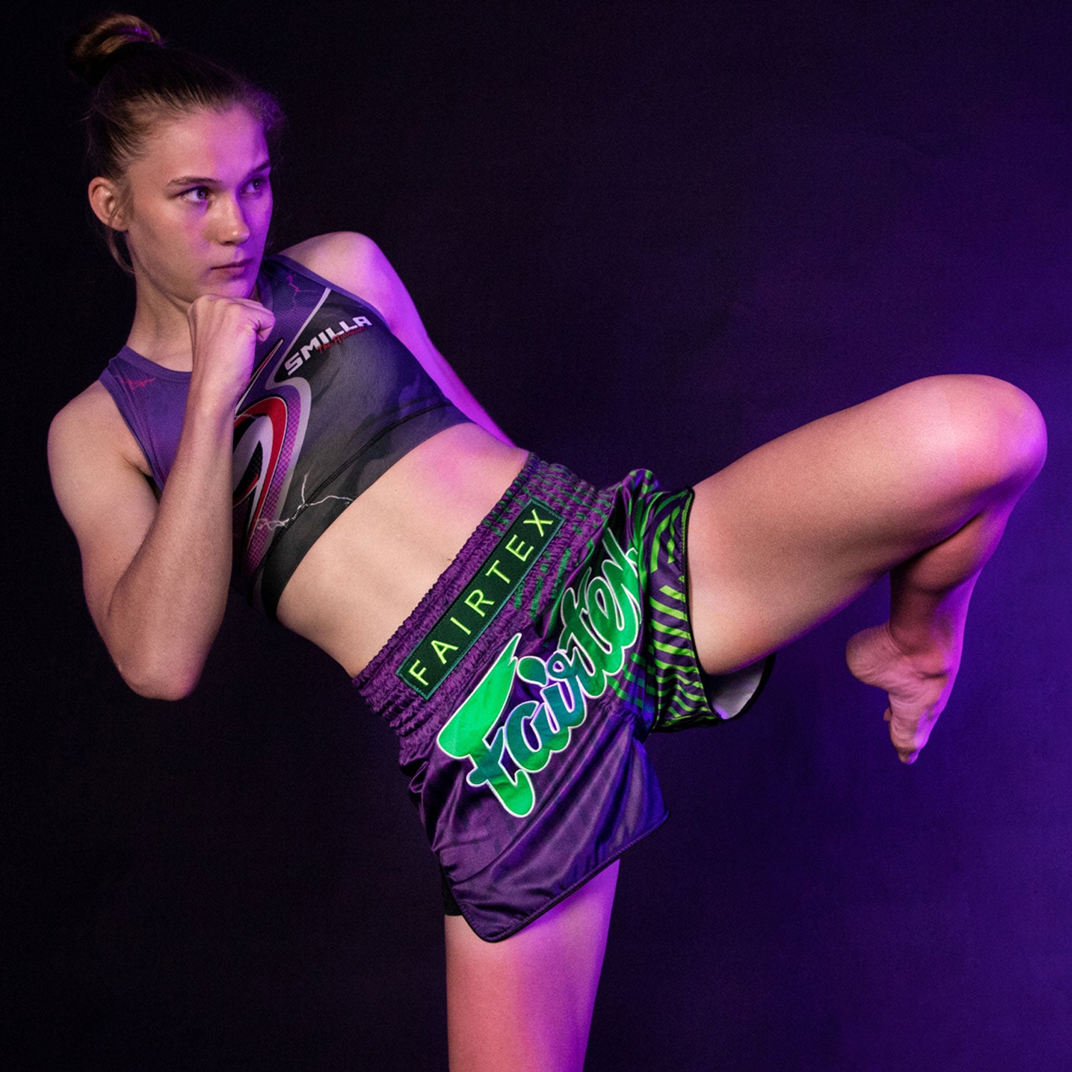 fairtex slim cut racer muay thai shorts purple with green stripes and green Fairtex logo model throwing a knee while wearing Fairtex Racer Shorts